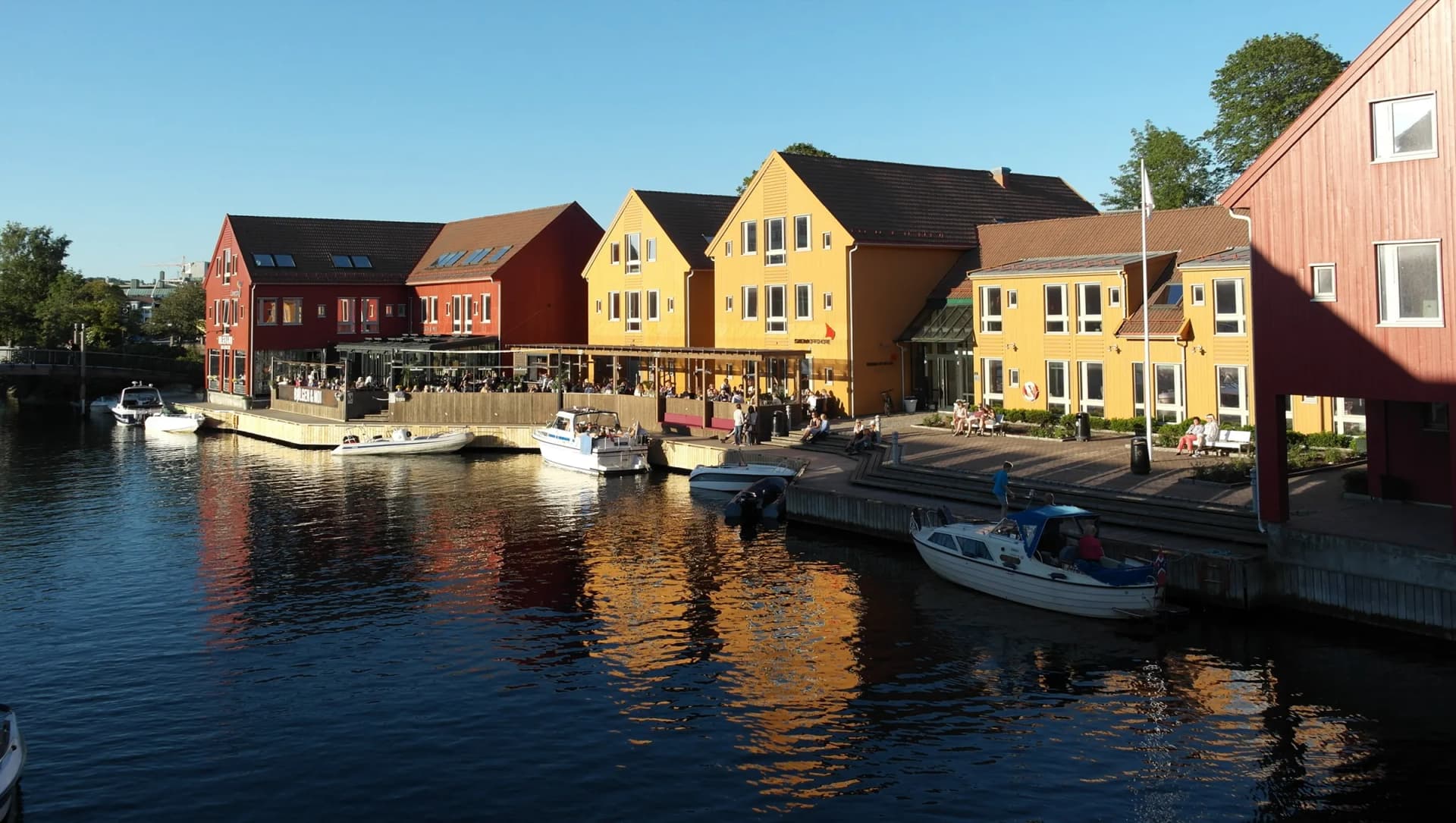 Fiskebrygga i Kristiansand i kveldssol — fargerike sjøhus og båter langs kanalen
