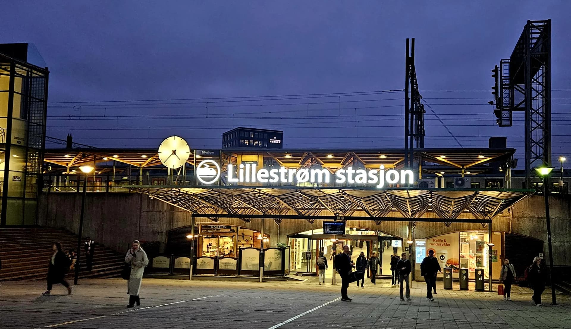 Lillestrøm stasjon i kveldslys med opplyst stasjonsskilt