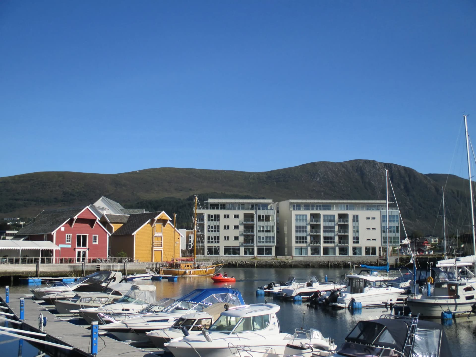 Småbåthavna i Ulsteinvik med fargerike sjøhus og fjell under blå himmel